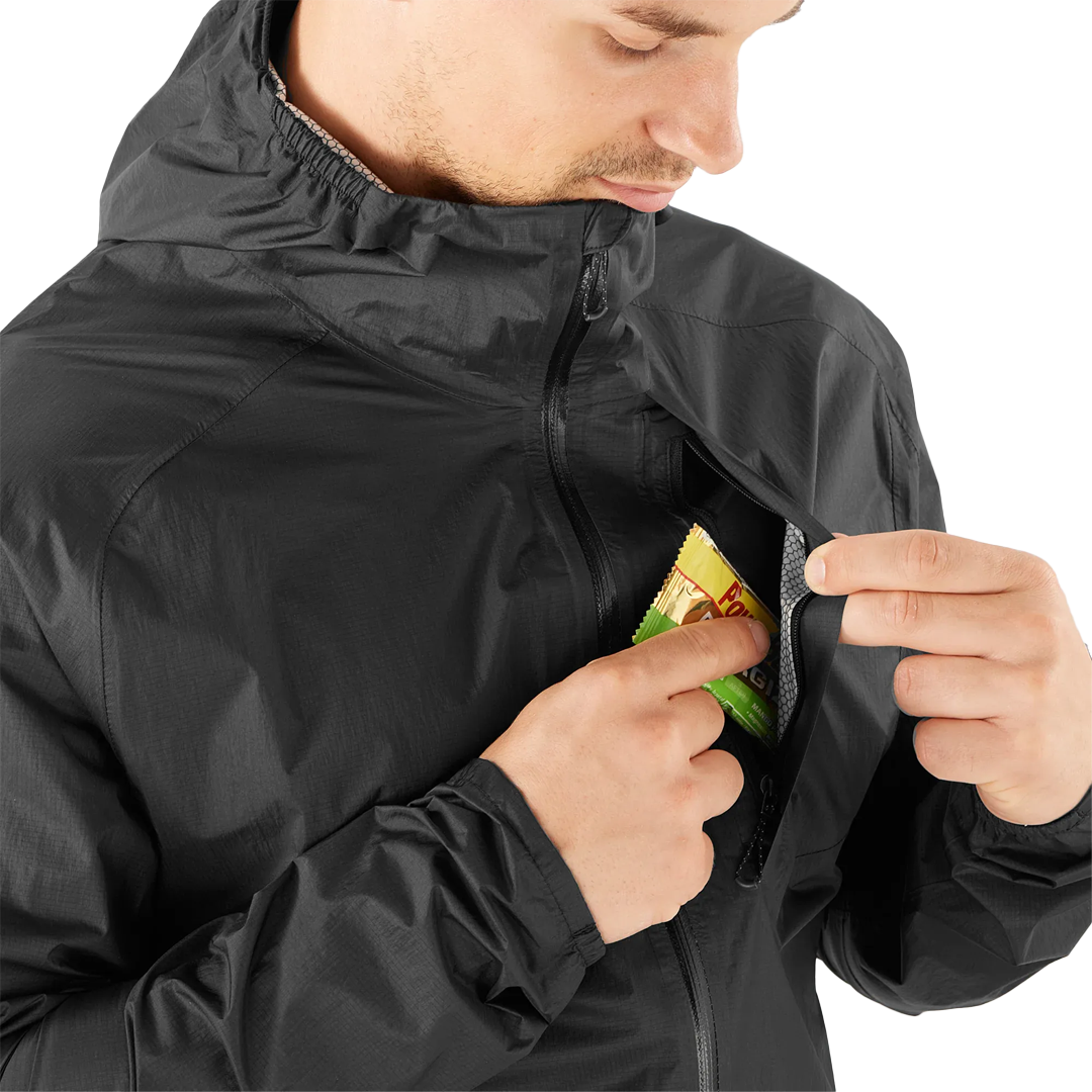 Person wearing a black jacket with a pocket, opening it to reveal a snack.
