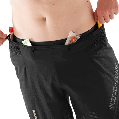 Person wearing black Salomon pants with items in the pockets on a white background