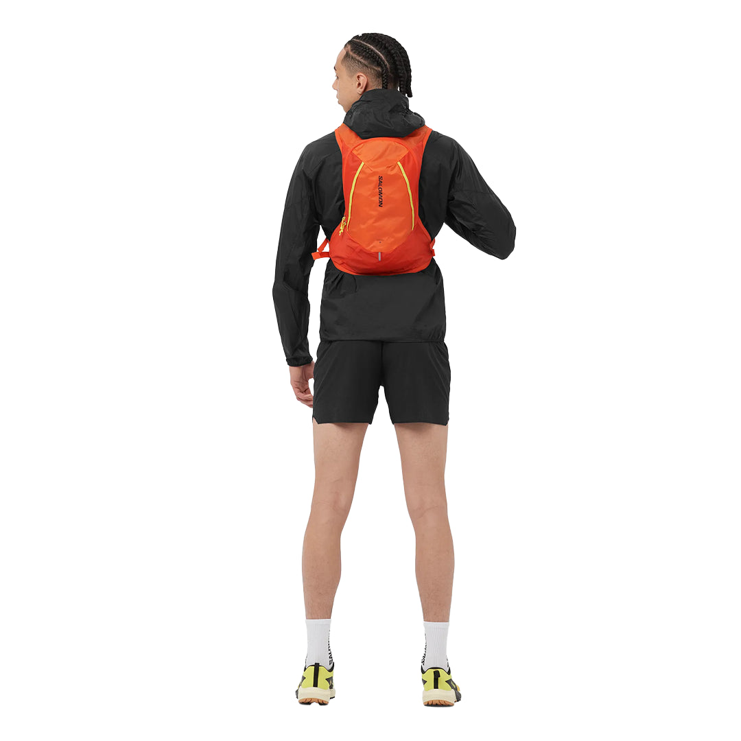 Person wearing a black jacket, black shorts, and an orange backpack on a white background